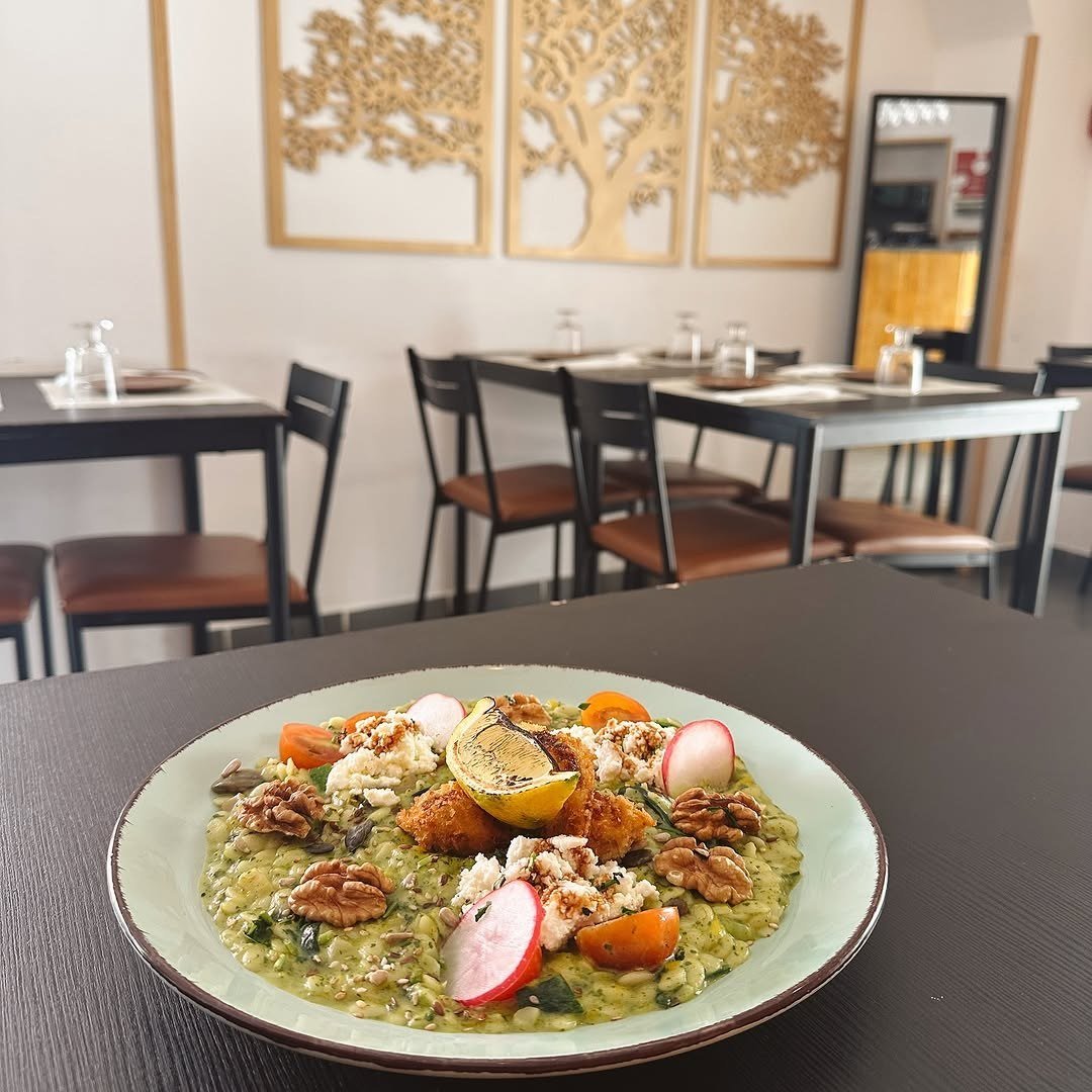 Prato de risotto verde com nozes, rabanete, tomate-cereja e limão grelhado, na sala do restaurante